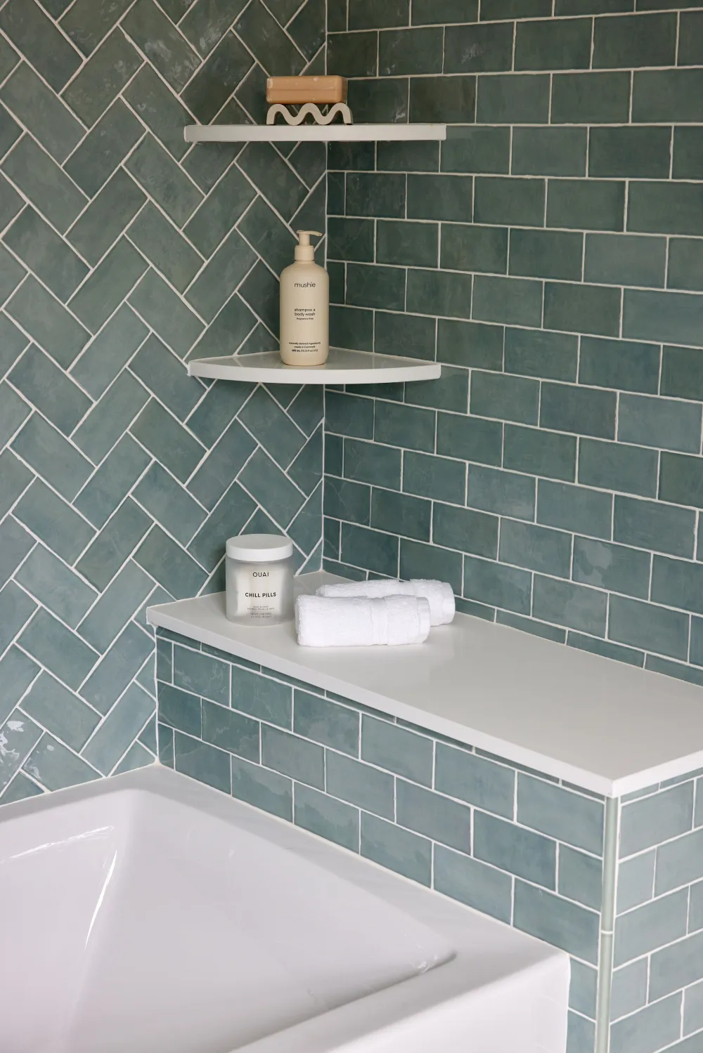 Green handmade-look subway tile shower with herringbone accent wall, white corner shelves, and built-in tub ledge in a real Tile America customer project.