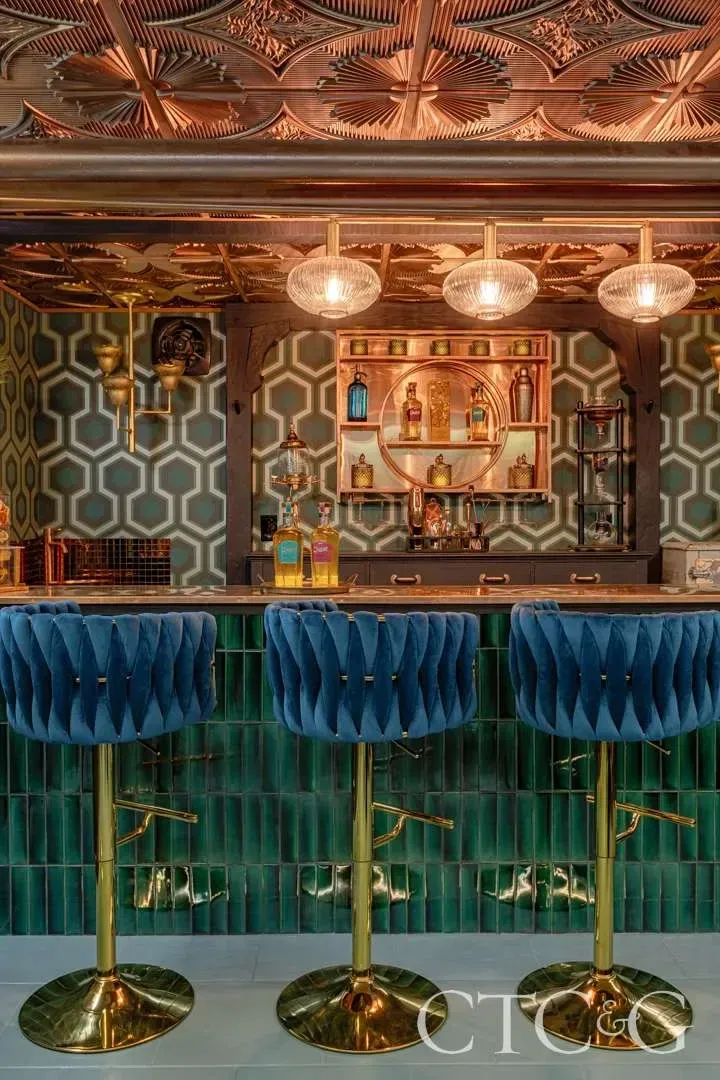 Upscale restaurant bar at Roli in New Haven featuring a green vertical stacked subway tile bar front, black penny round mosaic flooring, and navy blue barstools.