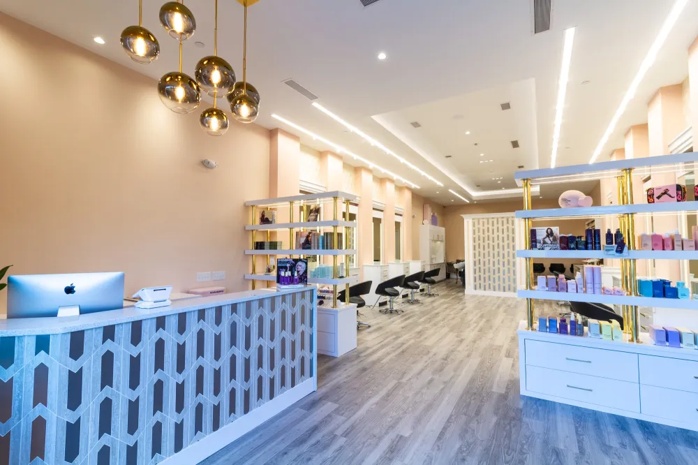Luxury hair salon reception desk clad in Audrey Lane Saturday Night geometric waterjet tile mosaic with wood-look floor planks and gold pendant lights.