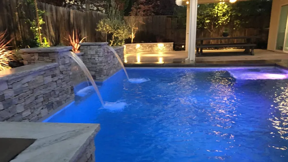 Backyard pool with Berkshire Buff Estate Stone cladding, water features, landscape lighting, and covered patio.