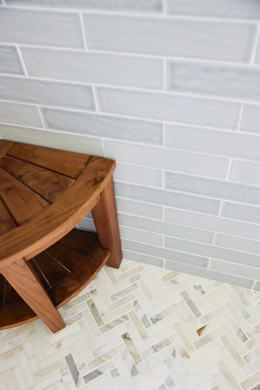 Walk-in shower detail showcasing a natural marble herringbone mosaic floor tile paired with light blue-grey subway wall tile.