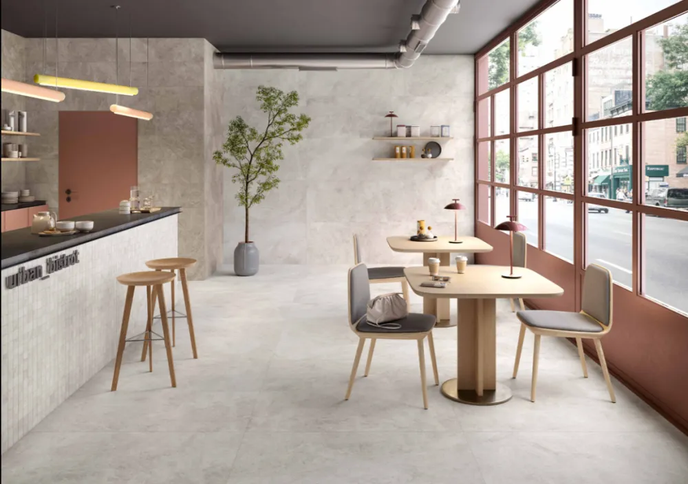 Modern commercial bistro cafe interior featuring Haven Milk 24x48 off-white stone-look porcelain floor and wall tiles with oak seating and terracotta window accents.