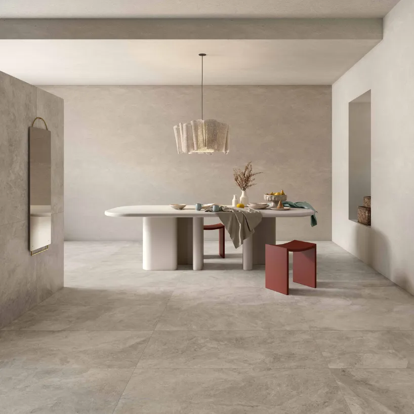 Minimalist dining room clad in Haven Shale 24x48 matte porcelain floor tiles featuring an oval white dining table and modern terracotta stools.