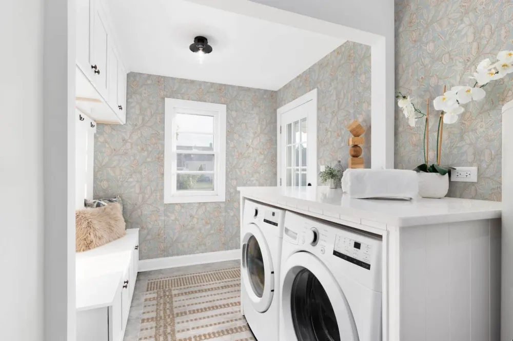 Bright laundry room and mudroom wrapped in Heirloom Blue botanical wallpaper with white cabinetry and laundry appliances.