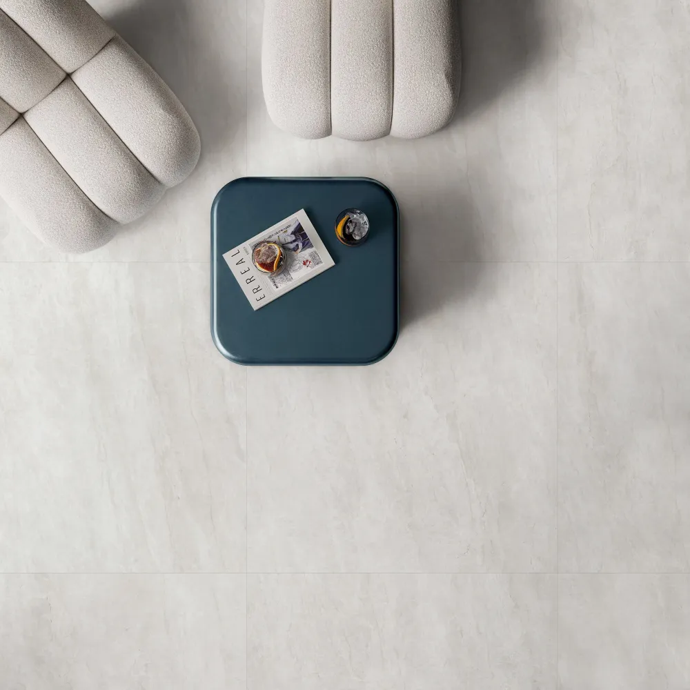 Overhead view of living room floor clad in Majestic Cotton off-white stone-look porcelain tile with channeled bouclu00e9 ottomans and a teal coffee table.