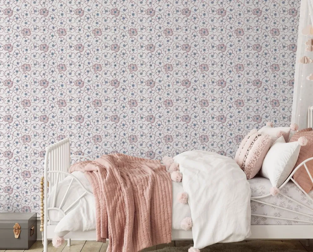 Kids bedroom feature wall clad in Petalpop Blush floral wallpaper behind a white iron daybed with pink pom-pom bedding.