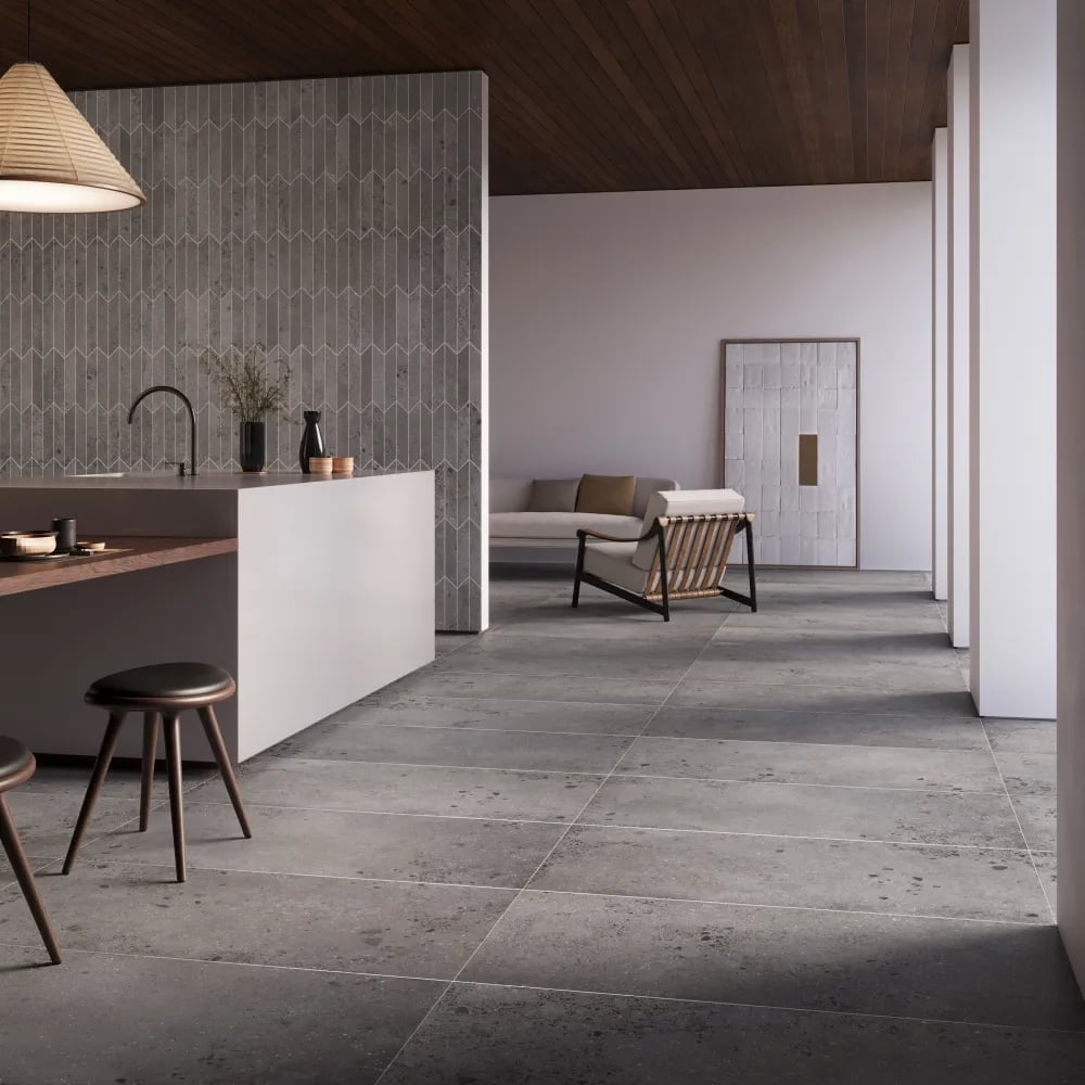 Modern open-concept kitchen floor clad in Lab Clay 24x48 concrete-look porcelain tiles with a vertical chevron mosaic wall backdrop.