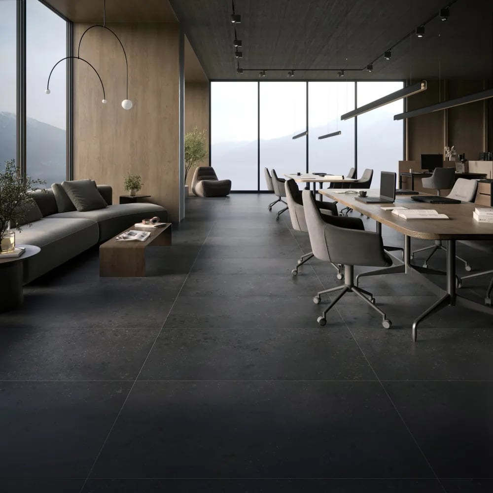 Modern office space featuring Lab Coal dark charcoal concrete-look porcelain floor tiles beside large glass windows and executive desks.