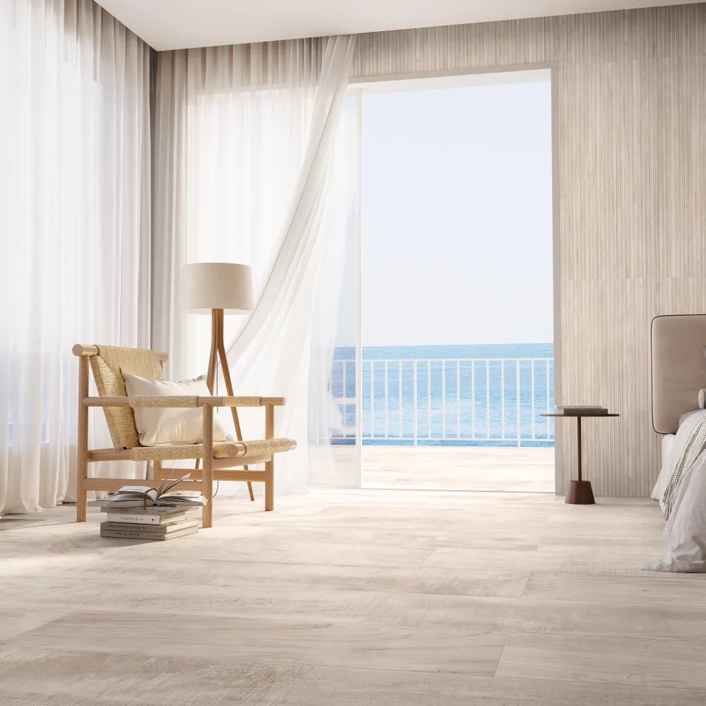 Bright coastal bedroom floor clad in Arca Alpine 8x48 light wood-look porcelain planks beside a fluted accent wall and balcony.