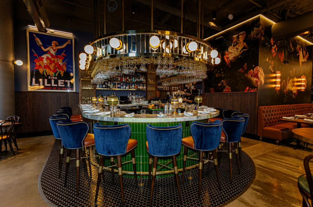 Upscale restaurant bar at Roli in West Hartford featuring a green vertical stacked subway tile bar front, black penny round mosaic flooring, and navy blue barstools.
