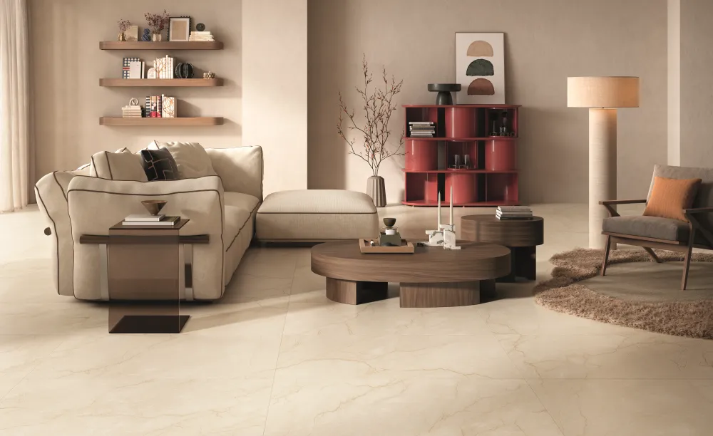 Modern living room floor clad in Sagrada Crema warm beige marble-look porcelain tiles with delicate golden-brown veining and a beige sectional sofa.