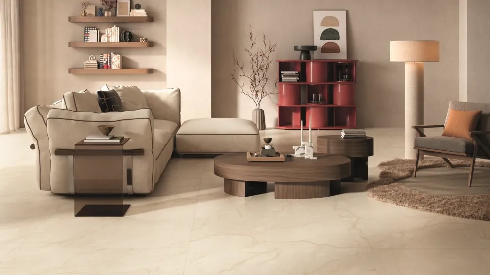Modern living room floor clad in Sagrada Crema warm beige marble-look porcelain tiles with delicate golden-brown veining and a beige sectional sofa.