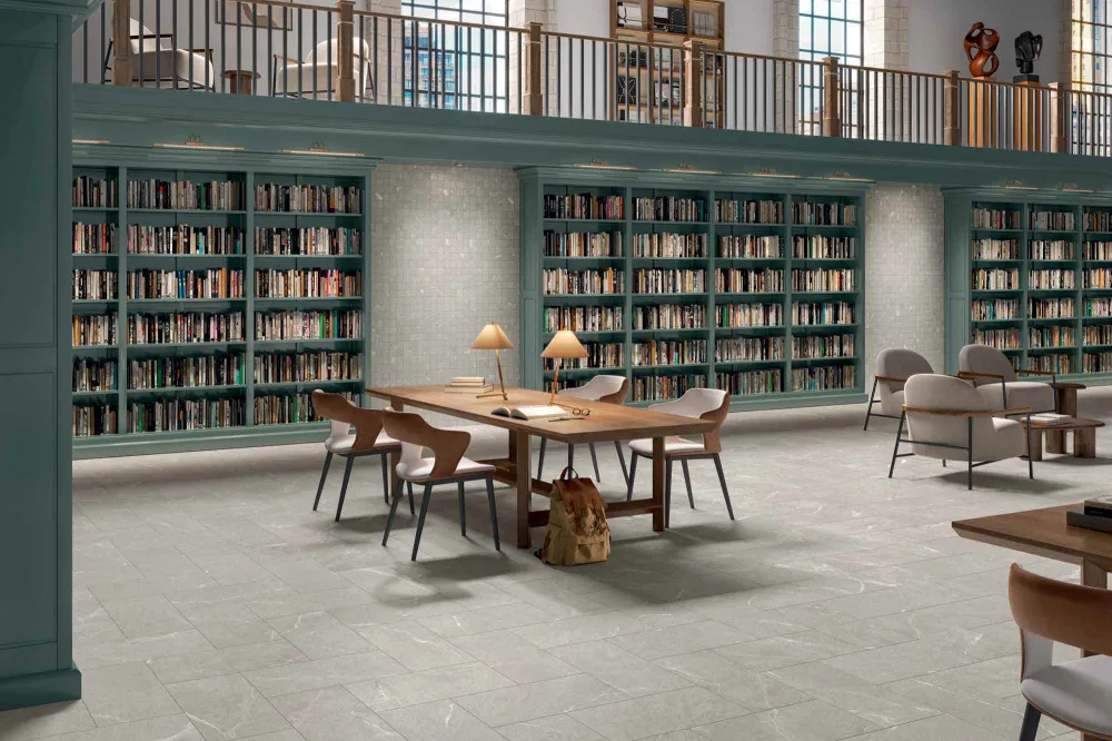 Two-story commercial library floor clad in Select Dolomite Gray stone-look porcelain tile with built-in teal bookshelves and wooden study tables.