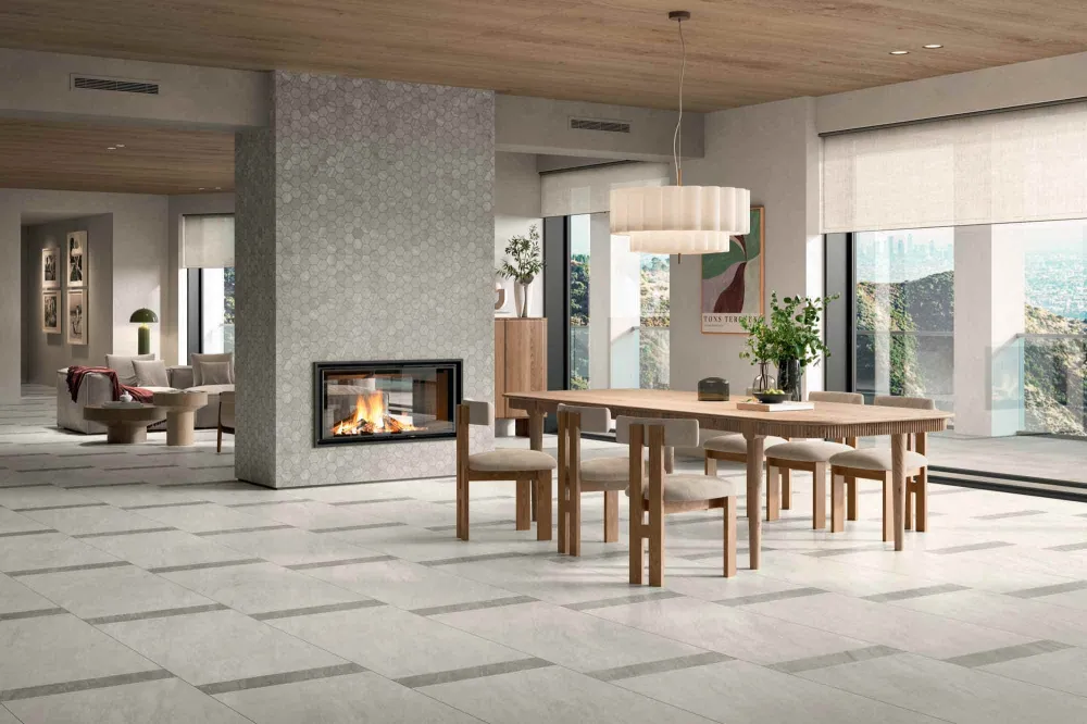 Open-concept dining and living room floor clad in Select Vanta White porcelain tile with Vanta Gray linear accents beside a hexagon mosaic fireplace surround.