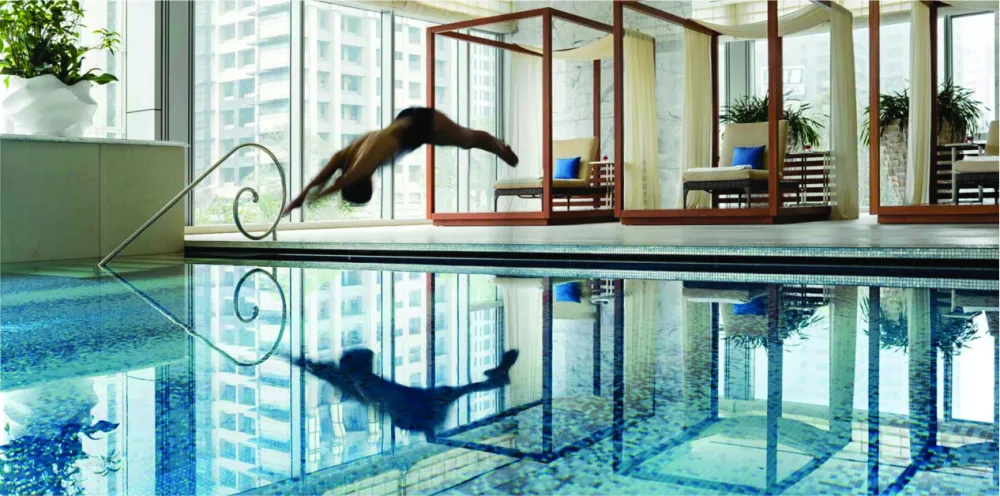 Luxury indoor swimming pool featuring blue Sicis glass mosaic tile, poolside cabanas, and floor-to-ceiling city views.