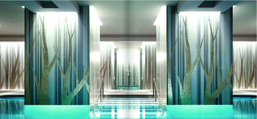 High-end indoor spa pool featuring artistic Sicis glass mosaic wall murals depicting metallic tree silhouettes with cove lighting.