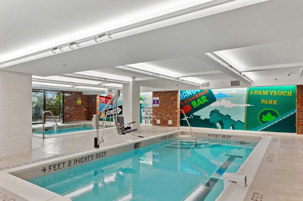Indoor swimming pool and spa facility at Torre House in Brooklyn featuring beige porcelain floor tile, white subway tile columns, and Brooklyn murals.