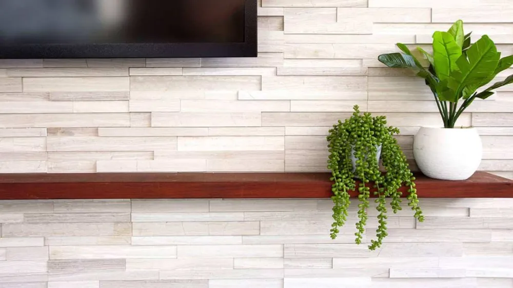 Close-up of White Birch Honed stone cladding behind an outdoor TV wall with wood shelf and greenery.