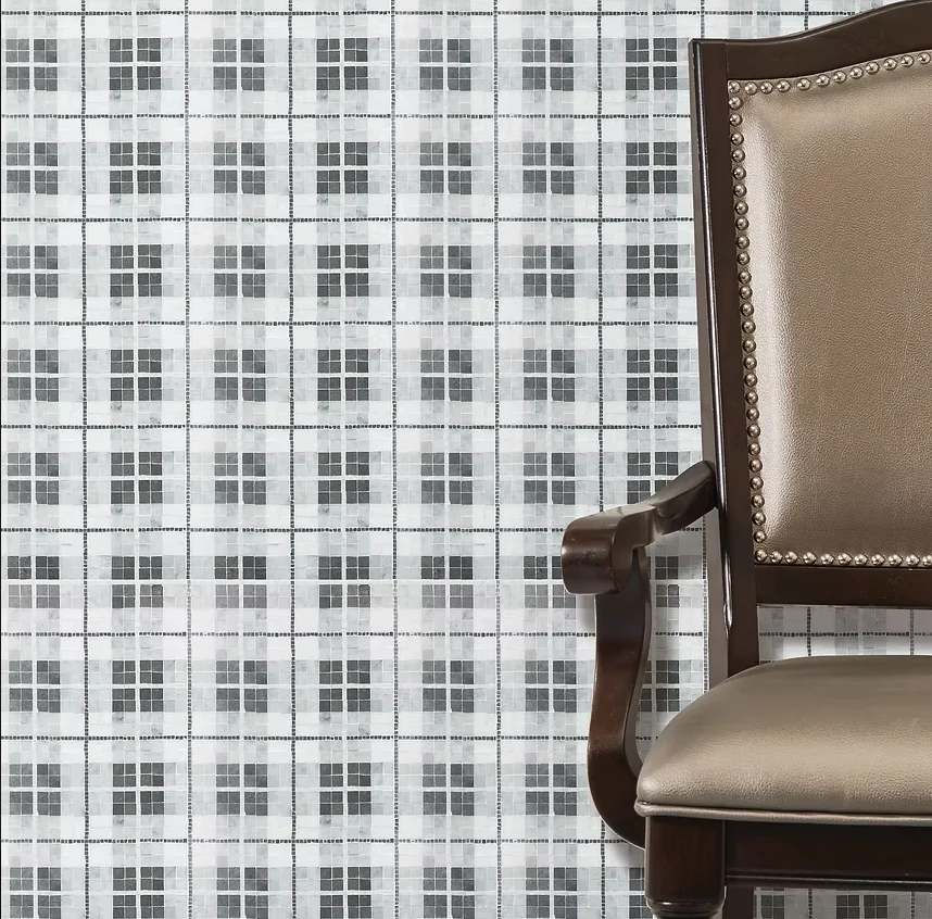 Brown leather-upholstered wooden armchair with nailhead trim beside gray-and-white small-square mosaic wallpaper.